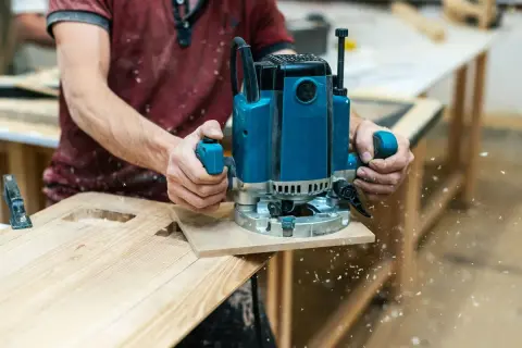 Un artisan utilise une défonceuse pour façonner du bois, créant des découpes précises. C'est une excellente démonstration de que faire avec une défonceuse pour des projets de menuiserie.