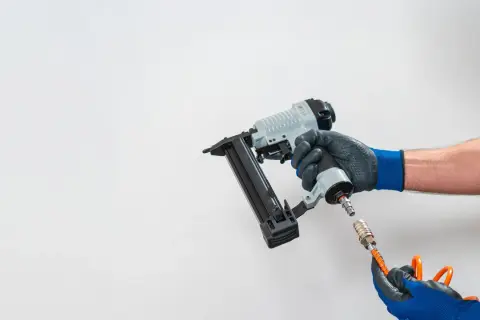 Main d'un bricoleur connectant un tuyau à un pistolet à clous pneumatique, un outil essentiel pour tout projet de menuiserie.