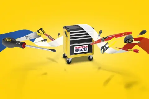 Boîte à outils jaune avec divers outils Stanley, dont une scie, des tournevis et un niveau. Le logo "Fabrication Française" est visible.