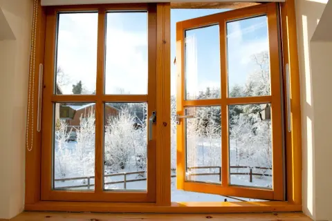 Une fenêtre en bois, prête à être poncée, s'ouvre sur un paysage hivernal enneigé.