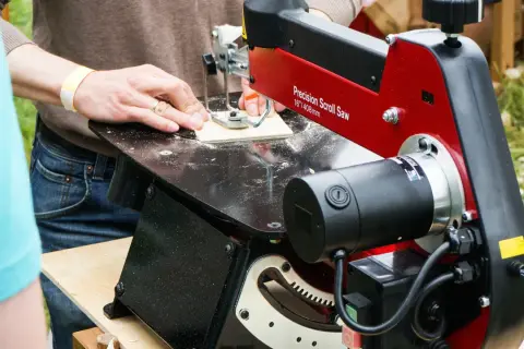 Un artisan utilise une scie à chantourner pour découper des formes complexes dans du bois. Cet outil permet de réaliser des détails fins et précis.