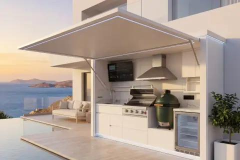 Une cuisine d'été fait maison moderne avec barbecue, évier, frigo et TV, surplombant la mer et une piscine.