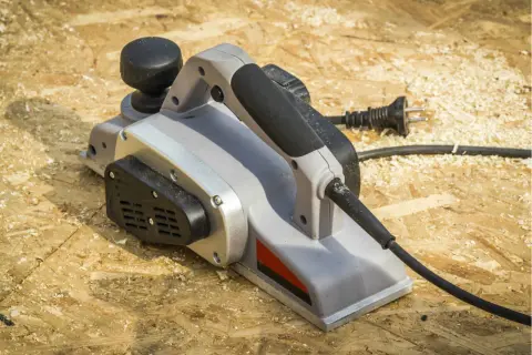 Une raboteuse électrique, prête à aplanir le bois, repose sur un chantier jonché de copeaux.