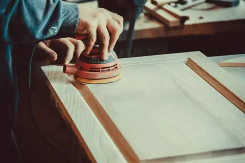 Un artisan utilise une ponceuse orbitale pour lisser une porte en bois. Le choix de la ponceuse est crucial pour un travail de finition parfait.