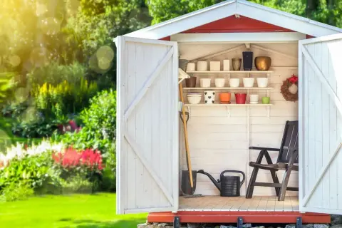 Aménagement abri de jardin : outils, pots de fleurs et chaise attendent le jardinier.