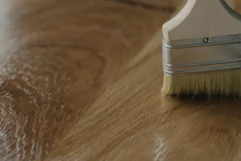 Application d'un vernis ou huile pour bois avec un pinceau sur une surface en bois.