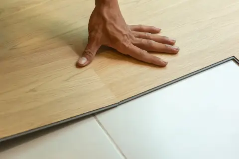 Pose d'un parquet stratifié imitation bois clair. Une main ajuste une lame sur un sol blanc.