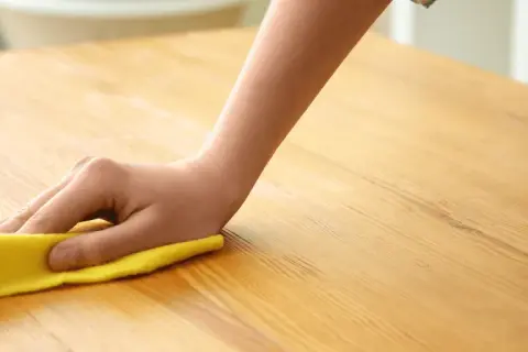 Main d'enfant nettoyant une table en bois avec un chiffon jaune. Apprenez comment nettoyer une table en bois pour un éclat parfait.
