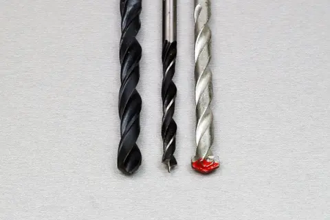 Trois forets de tailles différentes, dont un avec une pointe rouge, prêts à percer un chemin à travers un matériau, comme un foret dans un foret.