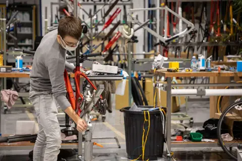 Un ouvrier assemble un vélo rouge, peut-être une création de la marque Korman, dans un atelier rempli de cadres.