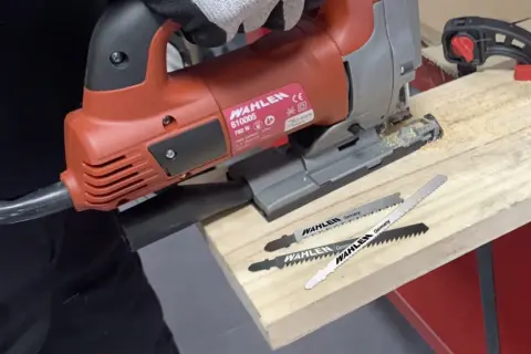 Lames pour reconnaître lame scie sauteuse métal. Une scie sauteuse rouge WAHLEN et trois lames sont posées sur une planche de bois.