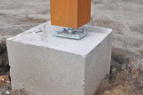 Un poteau en bois est fixé sur un plot béton à enterrer, prêt pour une construction solide.