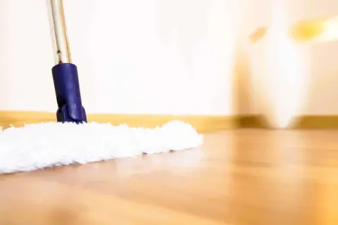 Une serpillère blanche et moelleuse nettoie un parquet brillant. La lumière douce éclaire la scène, créant une ambiance chaleureuse.