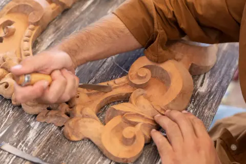 Un artisan utilise un ciseau pour sculpter le bois, créant des volutes complexes sur une pièce ornementale.
