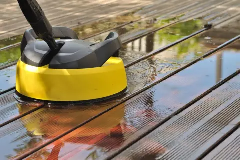 Nettoyer terrasse bois savon noir : un nettoyeur haute pression jaune et noir en action sur des lattes de bois mouillées.