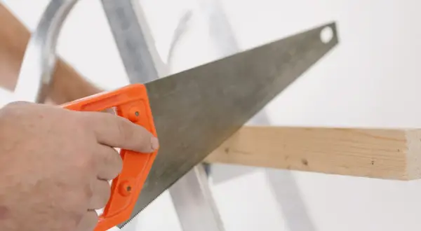 Main tenant une scie à bois à manche orange, coupant une planche. La différence scie à bois scie à métaux est dans la denture.
