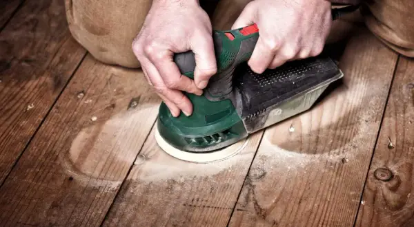 Mains tenant une ponceuse pour le ponçage du parquet. La poussière vole autour de l'outil pendant le travail.