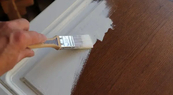 Application d'un vernis après peinture sur un meuble en bois. La main tient un pinceau pour appliquer la couche protectrice.