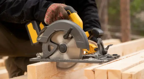 Main d'un bricoleur utilisant une scie circulaire pour couper du bois. La scie a une hauteur de coupe de 200 mm.