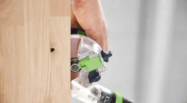 Main d'un artisan utilisant la défonceuse Festool OFK 500 pour travailler le bois avec précision.