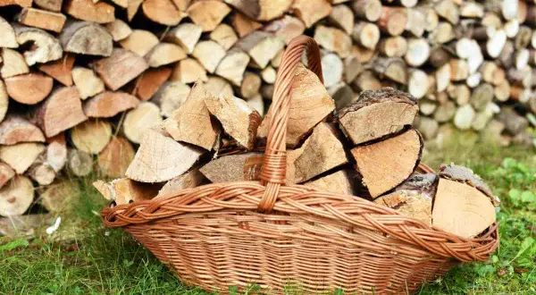 Panier en osier rempli de bois de chauffage, prêt pour le traitement du bois contre l'humidité. Le fond est un mur de bûches empilées.