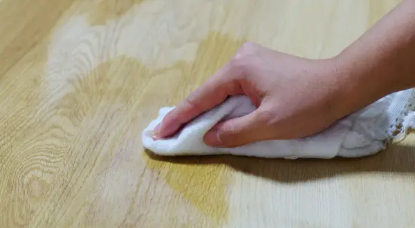Main d'une personne essuyant une tache d'huile sur un parquet en bois avec un chiffon blanc.
