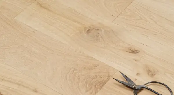 Un parquet en chêne clair, avec des ciseaux posés dessus. Peut-on laisser un parquet brut ? La réponse est oui, pour un style naturel.
