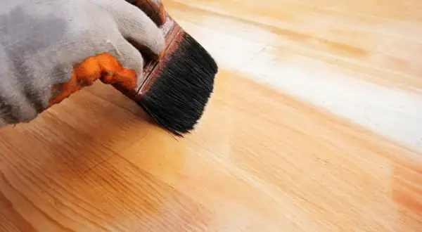 Main gauche gantée appliquant de l'huile de lin sur du bois. Attention, l'huile de lin peut présenter un danger d'auto-inflammation si mal stockée.