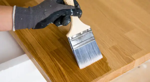 Application d'huile de lin au pinceau sur un plateau en bois. La finition protège et sublime le grain du bois.