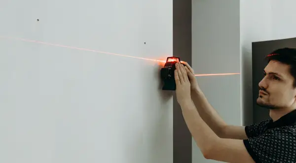 Un homme utilise un niveau laser pour tracer une ligne parfaitement droite sur un mur blanc.