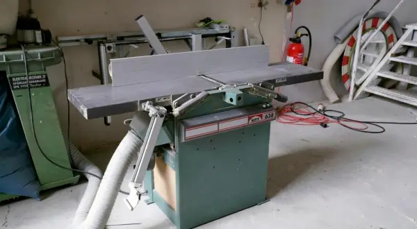Détail d'une dégauchisseuse KITY 638 dans un atelier, avec un aspirateur à copeaux et des câbles électriques à proximité.