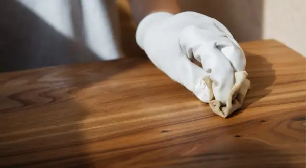Main d'une personne portant un gant blanc appliquant de l'huile de lin dure naturelle sur un meuble en bois.