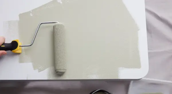 Application d'une peinture beige sur du mélaminé blanc avec un rouleau. Le résultat est une surface lisse et uniforme.