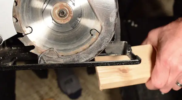 Démonstration de comment utiliser une scie circulaire pour couper du bois. La lame est prête à entamer le morceau de bois tenu par une main.