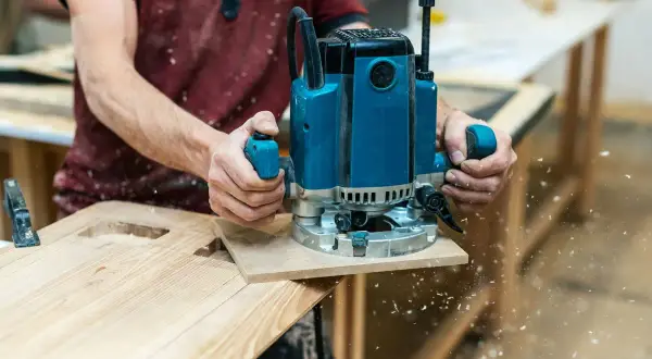 Un artisan utilise une défonceuse pour façonner du bois, créant des découpes précises. C'est une excellente démonstration de que faire avec une défonceuse pour des projets de menuiserie.