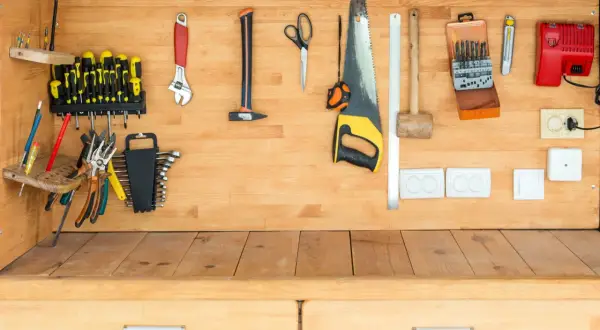 Un établi en bois bien rangé avec des outils : tournevis, clés, scie, marteau, ciseaux, et une boîte de forets.