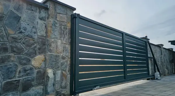Portail coulissant moderne en aluminium anthracite, juxtaposé à un mur en pierres naturelles. Le portail est en pose, prêt à sécuriser l'entrée.