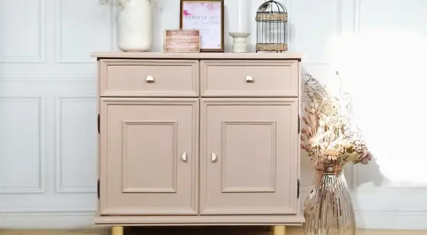 Un meuble en bois, fraîchement peint en rose poudré, est décoré de fleurs séchées et d'une cage à oiseaux.