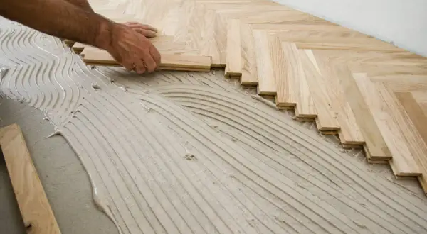 Pose d'un parquet en chevrons sur un lit de colle. Les lames de bois clair sont posées avec soin, formant un motif élégant.