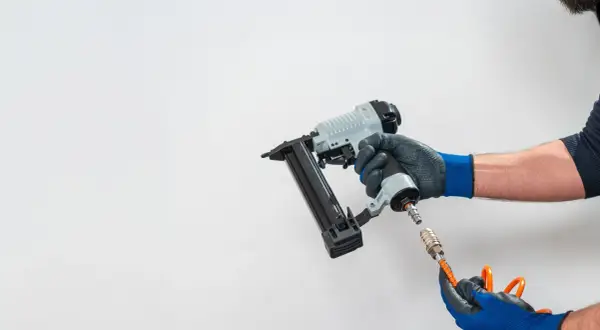 Main d'un bricoleur connectant un tuyau à un pistolet à clous pneumatique, un outil essentiel pour tout projet de menuiserie.