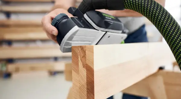 Main d'un artisan utilisant une raboteuse Festool pour lisser une pièce de bois.