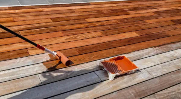 Application d'un saturateur sur une terrasse en bois exotique. Le rouleau dépose le produit, redonnant vie au bois.