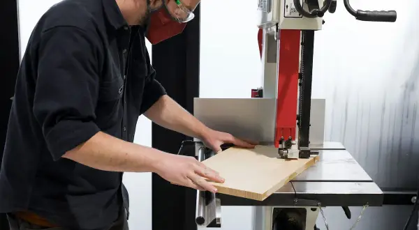 Un artisan utilise une scie à ruban, un des outils pour couper le bois, pour façonner une planche.