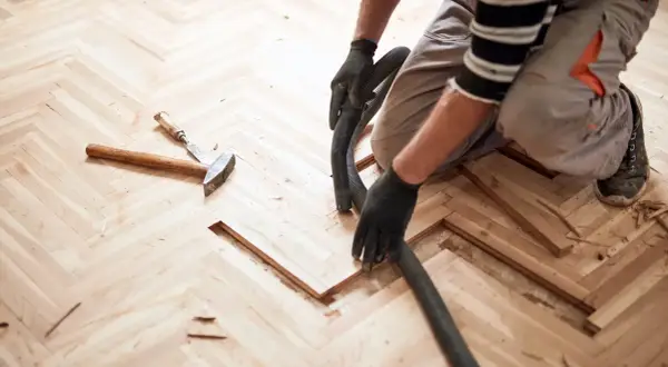 Un artisan utilise un aspirateur pour nettoyer la poussière de bois après le ponçage d'un parquet en chevrons. La pâte à bois blanchie au ponçage est prête pour la finition.
