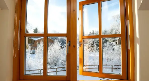 Une fenêtre en bois, prête à être poncée, s'ouvre sur un paysage hivernal enneigé.