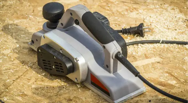 Une raboteuse électrique, prête à aplanir le bois, repose sur un chantier jonché de copeaux.