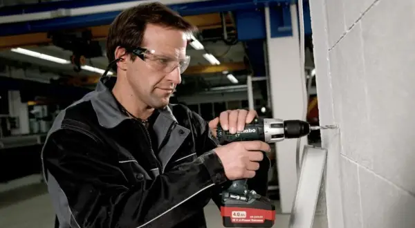 Un ouvrier utilise une perceuse sans fil Metabo, dont l'origine est allemande, pour percer un mur en parpaings.