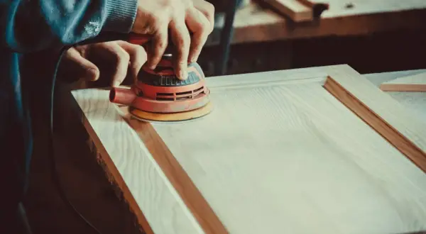 Un artisan utilise une ponceuse orbitale pour lisser une porte en bois. Le choix de la ponceuse est crucial pour un travail de finition parfait.
