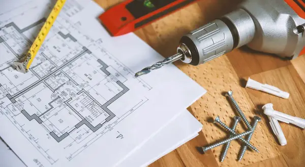 Plan de maison, mètre, vis, chevilles et perceuse de la marque Einhell, prêts pour le bricolage.