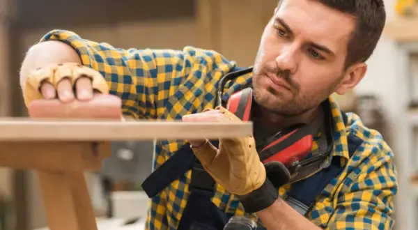 Artisan méticuleux, il s'applique à raboter une porte en bois avec soin.
